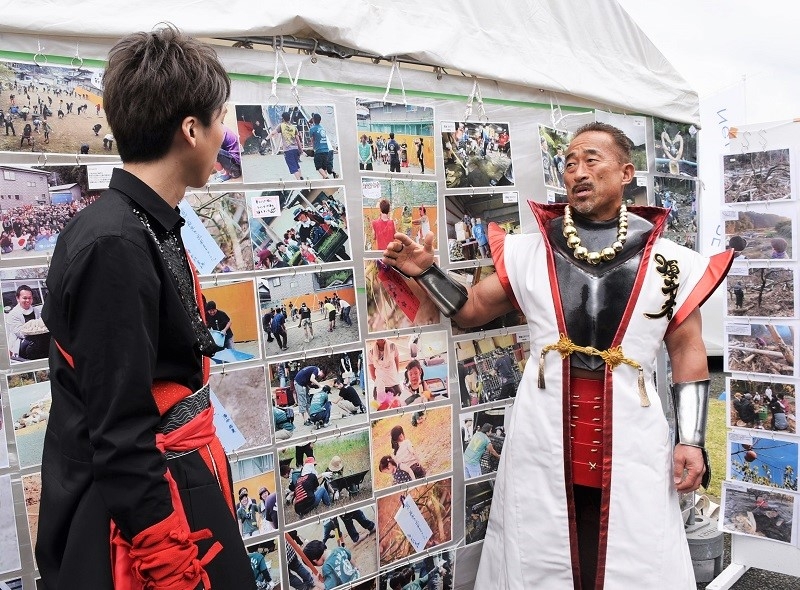 会場内に展示されていた被災地でのボランティア活動の写真を見る角田さんと大西さん。